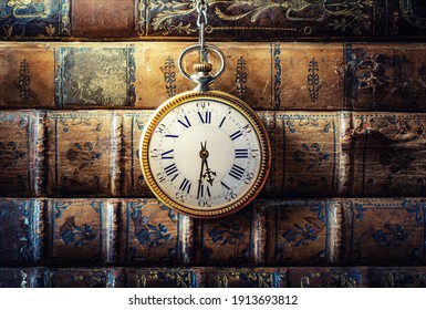 Vintage-Uhr hängt auf einer Kette auf dem Hintergrund alter Bücher. Alte Uhr als Symbol der Verlaufszeit. Konzept zum Thema Geschichte, Nostalgie, Alter. Retro-Stil.
