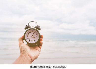 Vintage concept. Man hand hold alarm clock with blank screen with beautiful fresh sea sand and blue sky in the background. Vintage filter look.