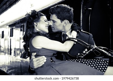 Vintage couple, man in uniform holding his sweetheart in his arms as they are about to kiss with train in background.