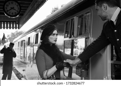 Vintage couple, man in uniform, woman in red dress, holding hands goodbye at train station as train is about to leave