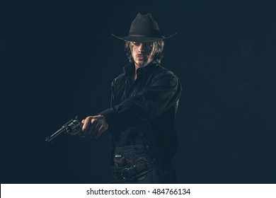 Vintage cowboy shooting with gun. Young man. Studio shot against dark wall.