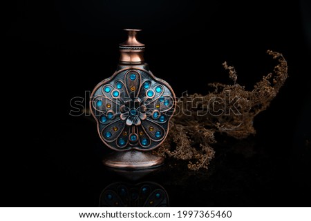 Vintage design bronze oud perfume bottle with sapphire blue gemstones on reflective black glass surface with black background.
