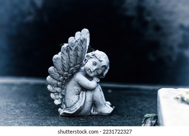 Vintage dirty statue of weep angel on tomb stone in old cemetery. Small ancient winged angelic figurine on dark sadness grave yard. Baby cherub figure symbol of consolation, grieve, belief protect - Powered by Shutterstock