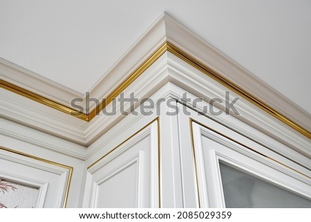 Vintage display case with crown molding and glass door in classic style and vintage wall panel with golden molding in light spacious room closeup