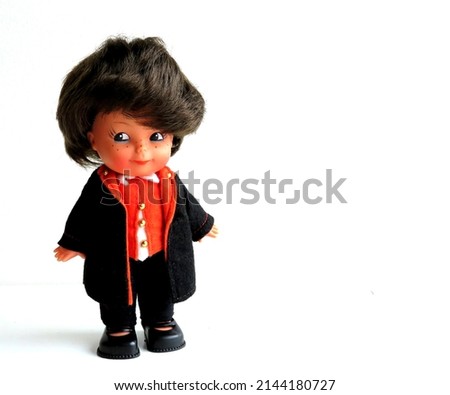 Vintage doll of boy with big eyes, freckles and big black hair. Dressed in a black and red circus ringmaster or orchestra conductor outfit. Isolated on white background with space for copy text.