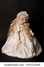 A vintage doll with golden-blond and curly hair sits on the table in a beautiful dress and a cap with lace. - Shutterstock ID 1911112345