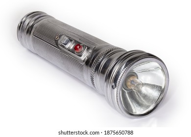 Vintage electric flashlight in metal fluted housing with two D size batteries and incandescent light bulb on a white background, close-up in selective focus