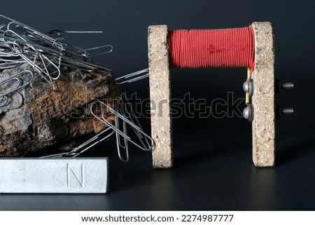 Vintage electromagnet with permanent north pole magnet and magnetite covered in paper clips to show magnetism. Black background. 