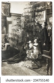 Vintage Family Portrait Of Parents And Child With Christmas Tree. Antique Picture With Original Film Grain And Blur. Black And White Photo