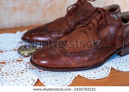 Vintage fashion style. Brown perforated leather brogue pair of shoes close-up. White crochet tablecloth. Retro bronze color compass. Gentleman style and accessories, nobleman stylish background. 