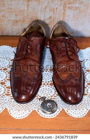 Vintage fashion style. Brown perforated leather brogue pair of shoes close-up, top view. White crochet tablecloth. Retro bronze color compass. Gentleman style and accessories, nobleman background. 