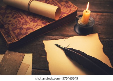 vintage feather with paper and old book on table in light of candle