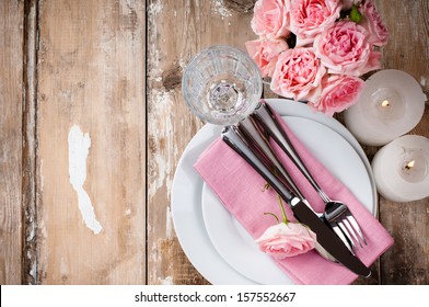 Vintage Festive Table Setting With Pink Roses, Candles And Cutlery On An Old Wooden Board