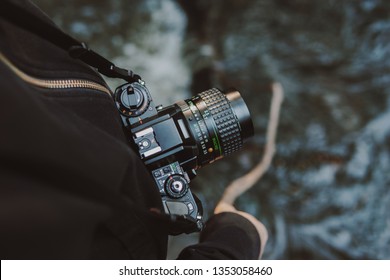 Vintage film camera around woman neck while she holds a stick into a river. - Powered by Shutterstock