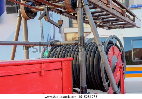Vintage fire and rescue equipment. A fragment of aged \
equipment (rolled fire hoses and wooden fire ladder) closeup on a \
red  fire truck 