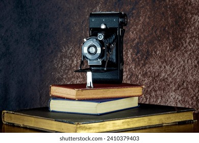 Vintage folding film camera on a pile of old books on a wooden shelf - Powered by Shutterstock