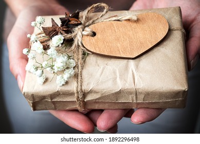 Vintage gift box wrapped in craft paper decorated with wooden heart and white flowers in human hands. Valentine day celebrating.  Selective focus - Powered by Shutterstock