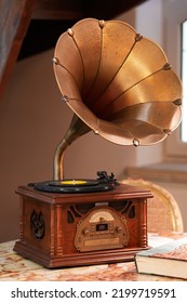 Vintage Gramophone Turntable With Brass Horn And Vinyl Disc Record On A Wooden Table Inside An Antique Place. Music As It Was Listened Years Ago.