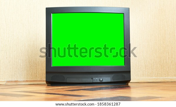 A vintage green\
screen TV sits on a wooden parquet floor, an antique design in an\
1980s and 1990s style house.