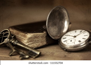 Vintage grunge still life with pocket watch, and old book and brass keys.