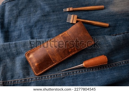Vintage Handmade Leather pencil case. Leathercraft tools with a denim background.	