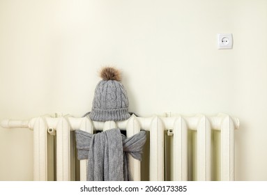 Vintage heating radiator with wool knitted winter hat and scarf. The electricity and gas bill goes up, European energy crisis concept. Background copy space, room for text.
