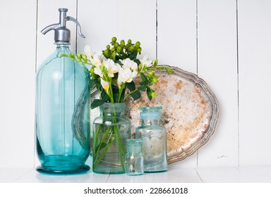 Vintage Home Decor, Ancient Turquoise Siphon, Freesias Bouquet And Bottles On A White Wooden Background.