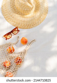 Vintage inspired background with straw hat, female sunglasses and shopper bag with peaches on white towel. Minimalist summer vacation creative still life ​for fashion blog, web, social media, stories.