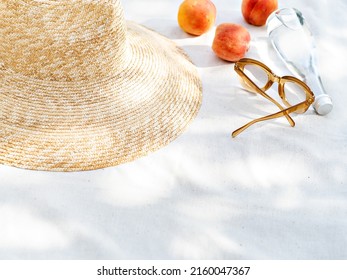 Vintage inspired background with straw hat, female sunglasses, bottle of water  and fruits on white towel. Minimalist summer vacation creative still life ​for fashion blog, web, social media, stories.