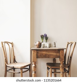 Vintage Interior Design Of Kitchen Space With Small Table Against White Wall With Simple Chairs And Plant Decorations. Minimalistic Concept Of Kitchen Space.