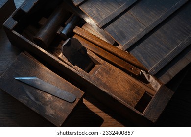 Vintage Japanese wood working toolbox with lid half open.  old rustic block planes and hammers. Japanese block planes, chisels and hammers in box. Intentionally shot with low key shadows. 