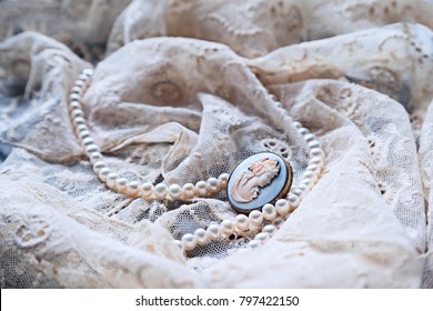 Vintage Jewelry On Old Cream Lace Textile. Pearl Necklace And Cameo Brooch.