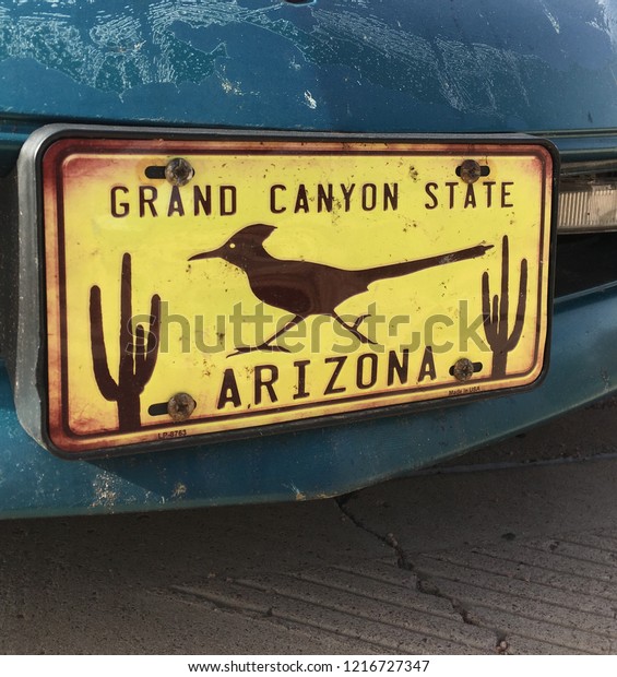 Vintage license\
plate that reads:  Grand Canyon State, Arizona with images of\
cactus and roadrunner on blue\
car