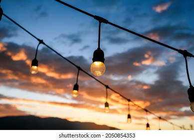 Vintage Light Bulbs On String Wire Against Sunset Sky Decor In Outdoors Wedding Event Party