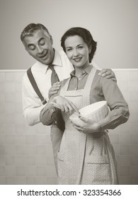 Vintage Loving Couple At Home, She Is Wearing An Apron And Cooking