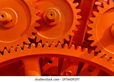 Vintage machinery cogwheels of a stone crusher in a decommissioned cement plant painted in striking orange color