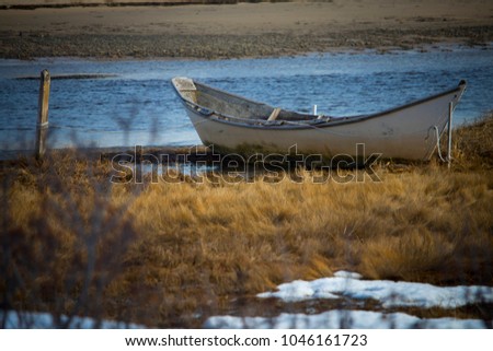 A vintage Maine dory boat moored to a wooden post along the shoreline in a salt marsh in Ogunquit, Maine.