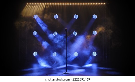 Vintage metal microphone looms against smoke and black studio background. An old concert microphone on an empty smoky dark stage illuminated by blue spotlights. Theater stage, concert performance.