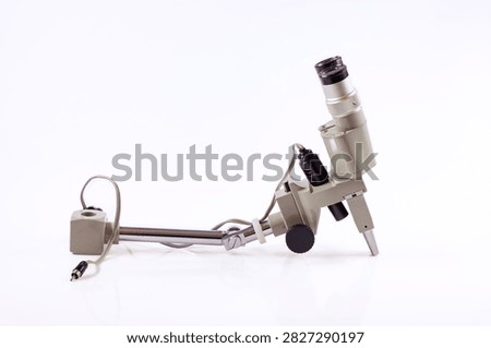 Vintage microscope head and support arm with eyepiece, focusing knob and electrical cable isolated on a white background.