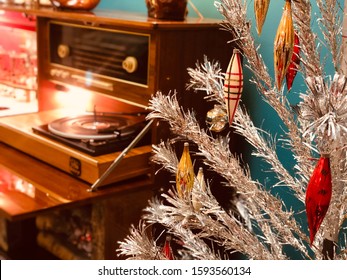 A vintage mid century modern close up of a silver tinsel tree with ornaments. A record player can be seen in the background.