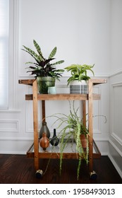 Vintage Mid Century Wooden Bar Cart Plant Stand Full Of Plants And Pottery Against A White Wall In A Victorian House