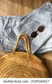 Vintage Mom Jeans, Round Straw Bag And Sunglasses On Wooden Background. Flat Lay.