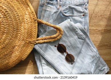 Vintage Mom Jeans, Round Straw Bag And Sunglasses On Wooden Background. Flat Lay.