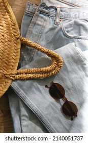 Vintage Mom Jeans, Round Straw Bag And Sunglasses On Wooden Background. Flat Lay.