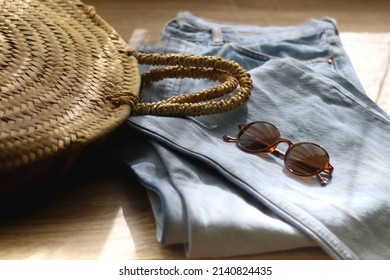 Vintage Mom Jeans, Round Straw Bag And Sunglasses On Wooden Background. Selective Focus.