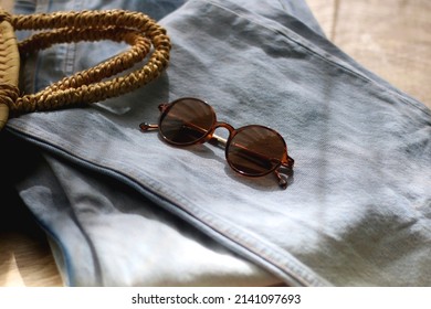 Vintage Mom Jeans, Round Straw Bag And Sunglasses On Wooden Background. Selective Focus.