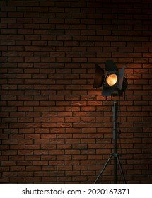 Vintage movie set spotlight lamp with fresnel lens and barndoors in front of red brick wall good as background for production, and moviemaking company
