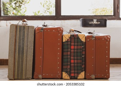 Vintage Old Classic Outdated Leather Suitcases In Interior Of Bright Room By Windows. Background With Suitcases Of Various Designs And Colors. Let's Sit On Path! Concept Luggage For Travel. Copy Space