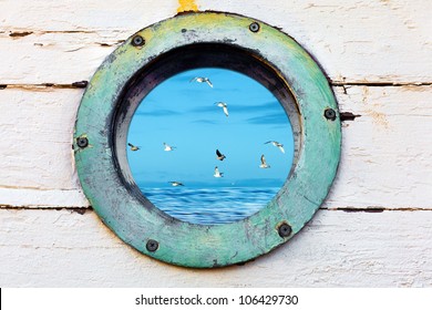 Vintage old porthole window with a view of the ocean and birds flying by.
