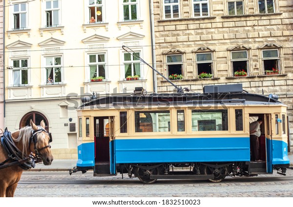 Vintage old tram and\
horse at old town market square in Lviv, Ukraine. Blue electric\
train driving, side\
view